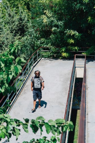 a man walking down a pedestrian bridge, trees around.