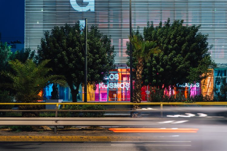 the colourful entrance of a buiding, trees and the a car on move.