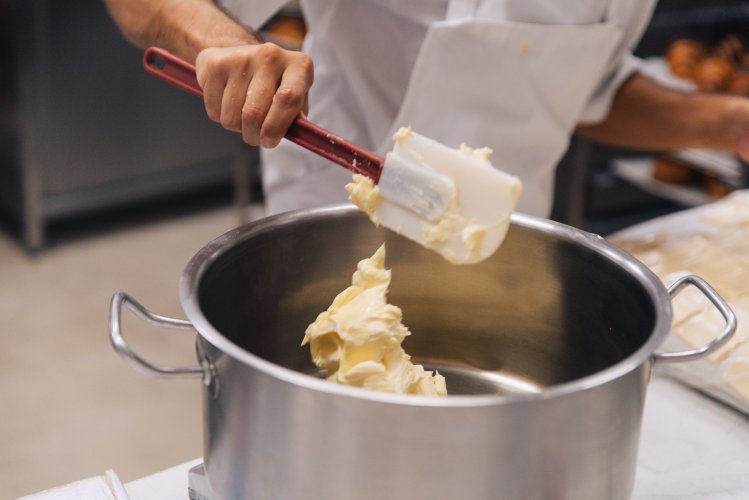 a pastry chef mixing butter with cream in a bowl using a silicone mariz.