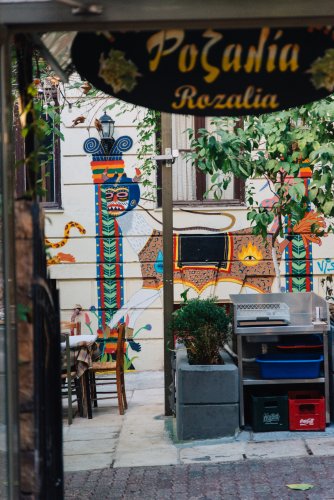 colourful murals on a wall, outdoor tables, a wooden sign that reads "Rozalia"