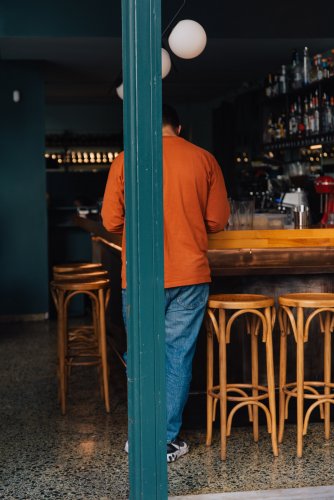 a man in a red blouse behind a column, in front of a bar