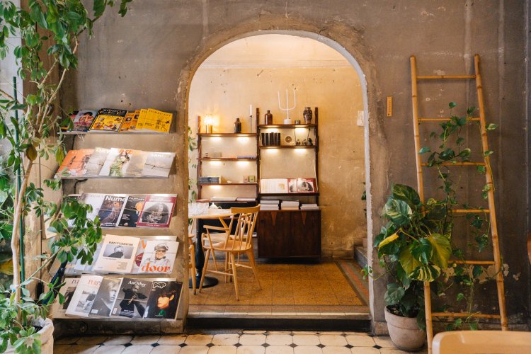 interior of a coffee shop, tables, chairs, plants and bookcases.