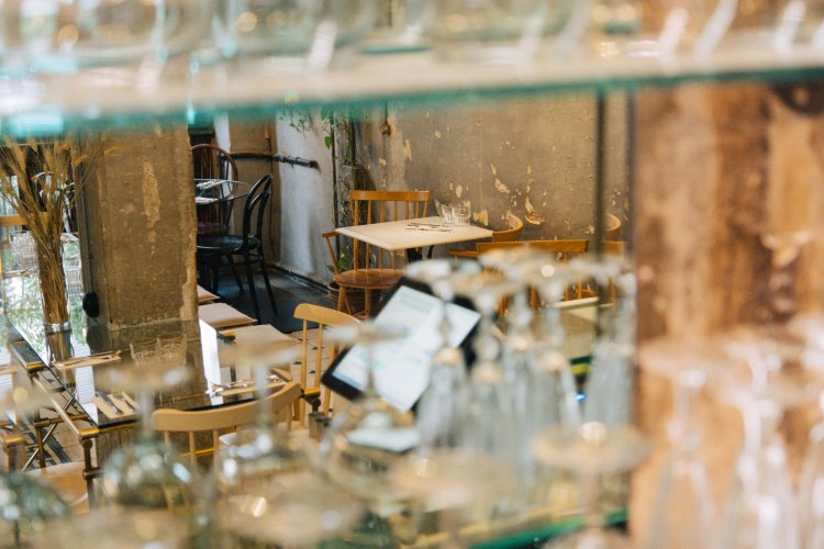 the interior of a brunch place, tables and chairs around, clean glasses on shelves.