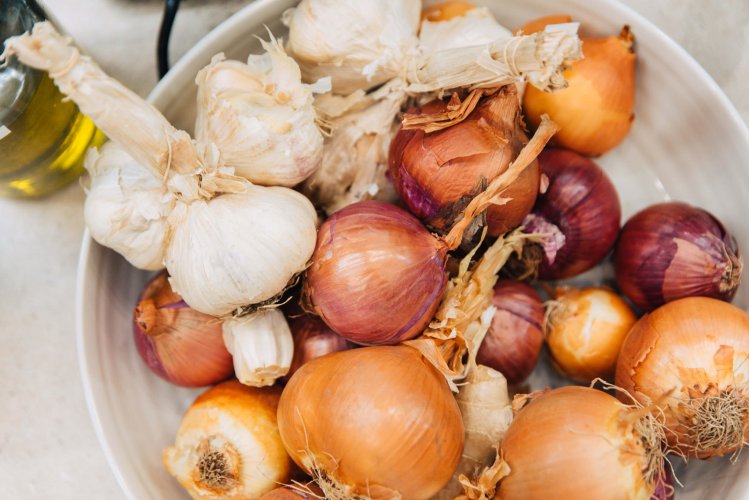 A white bowl filled with onions and garlic cloves.