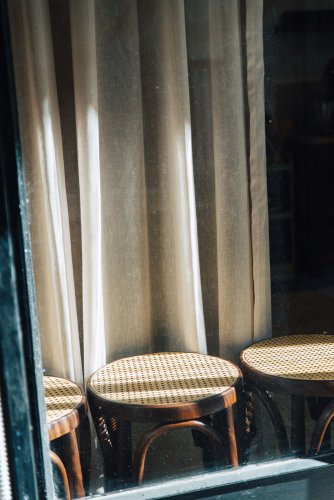 Three wooden stools, sunlight streams through a window behind them. A white curtain hanging
