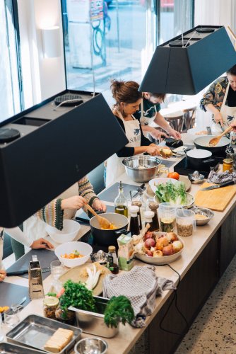 people cooking at a counter full with ingredients and utensils.