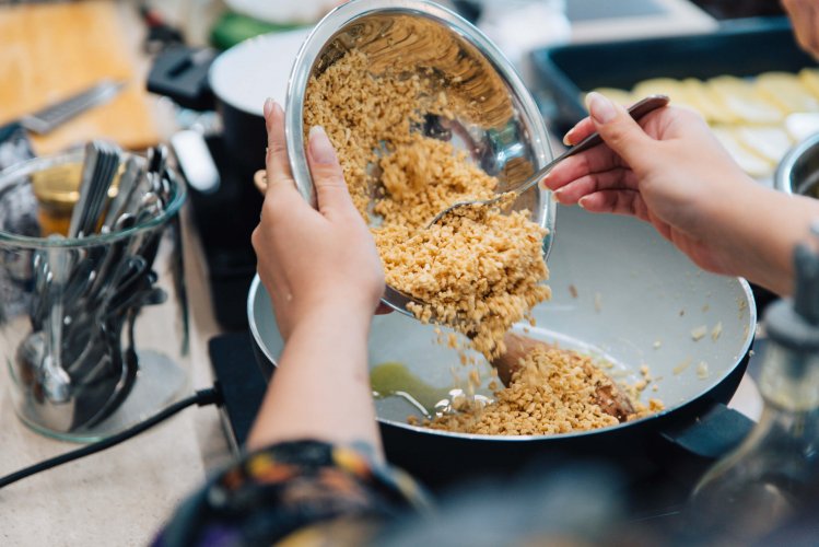 A woman pouring soya mince from a metal bowl into a pan.