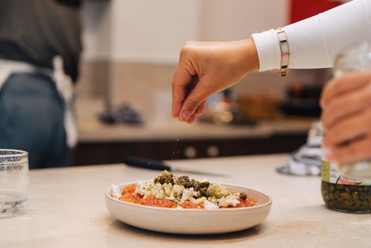 A woman sprinkling oregano on a salad on a dining table.