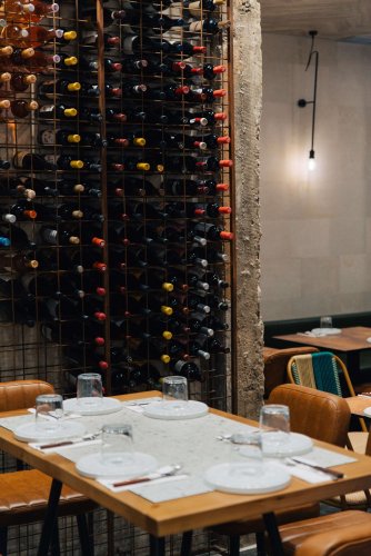 A set table at a restaurant, a large wine rack filled with wine bottles next to it.