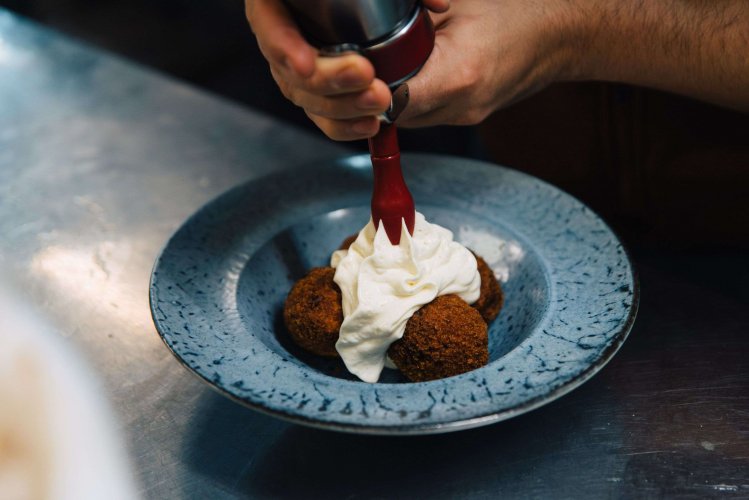 a man adding yogurt mouse on top of four meatballs