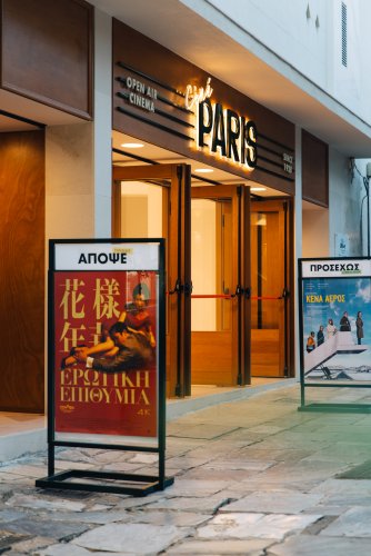 A brightly lit sign in front of an open-air cinema that reads "cine paris" and two movie posters