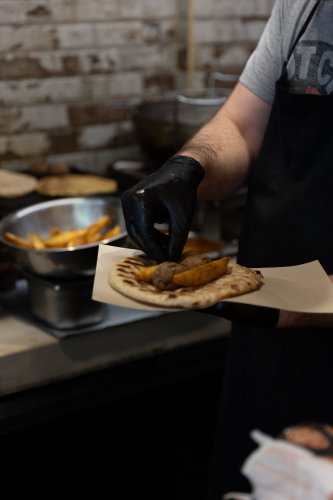 a chef adding potatoes next to a kebab in a pita bread.