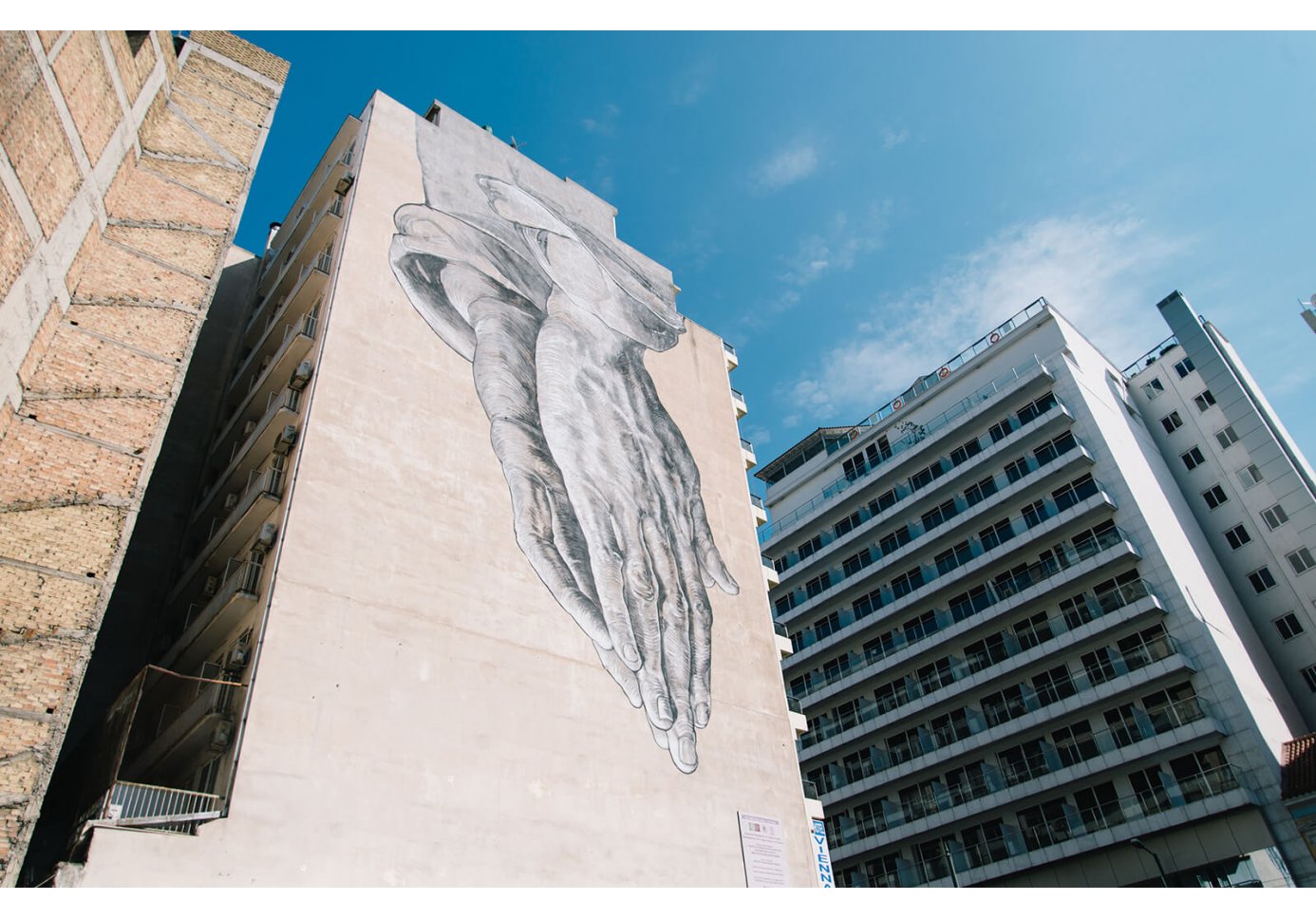 Graffiti of two hands joined in prayer on a building facade 