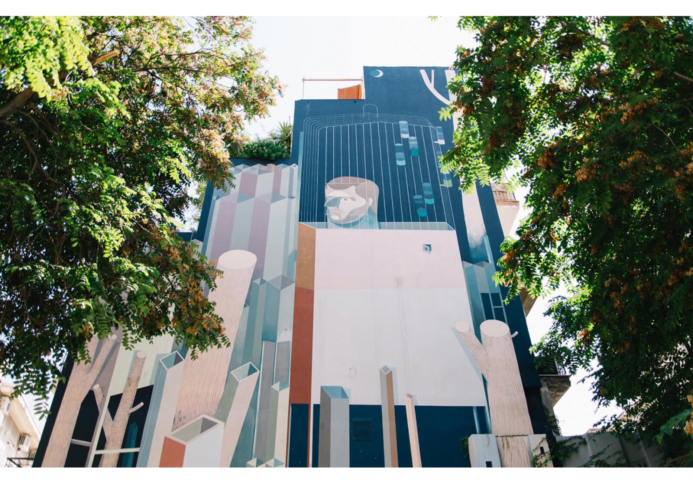 Graffiti of a man's head in a box on a building in between two trees.