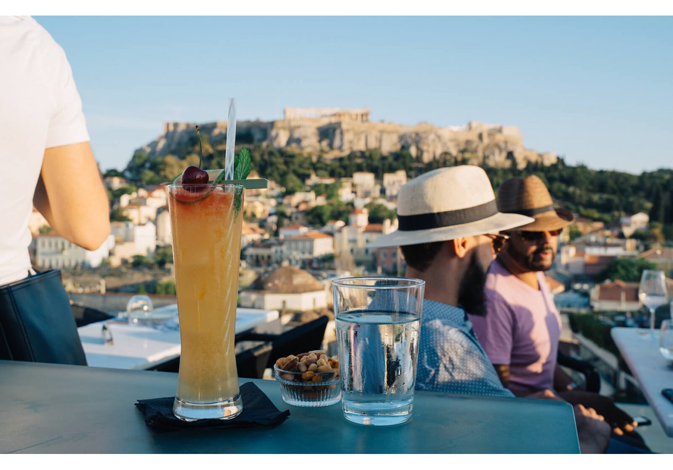 A drink and people sitting at A for Athens cocktail bar with view of Acropolis.
