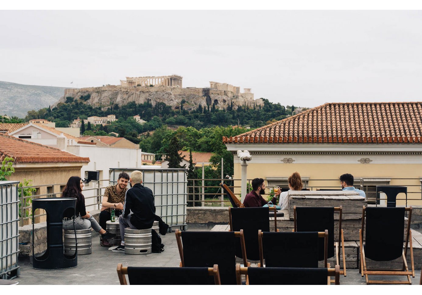 People sitting at the rooftop bar at bios in Athens with a view of the Acropolis. 