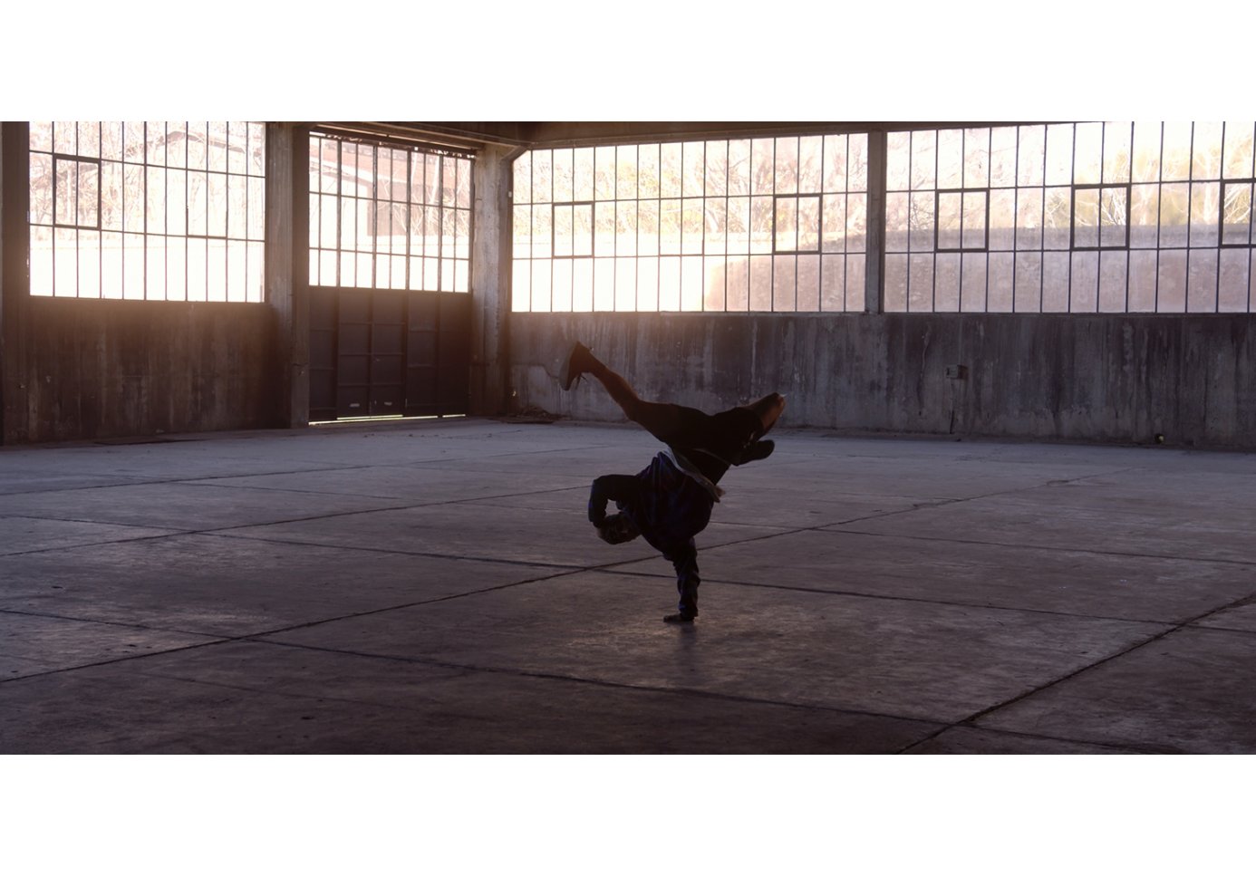 A man breakdancing in an empty warehouse