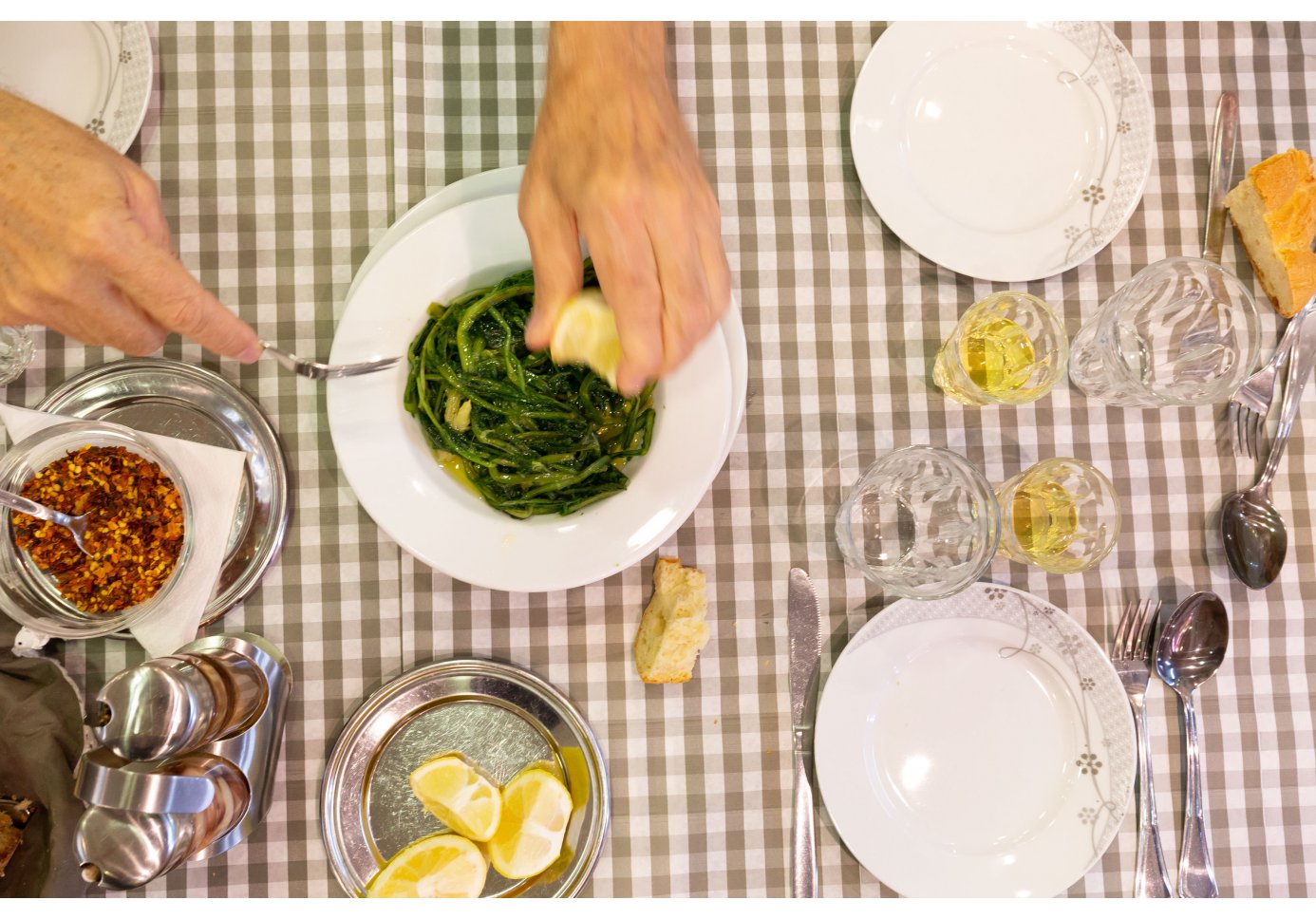 A man squeezing lemon over a dish of greens in Ipirus taverna in Athens
