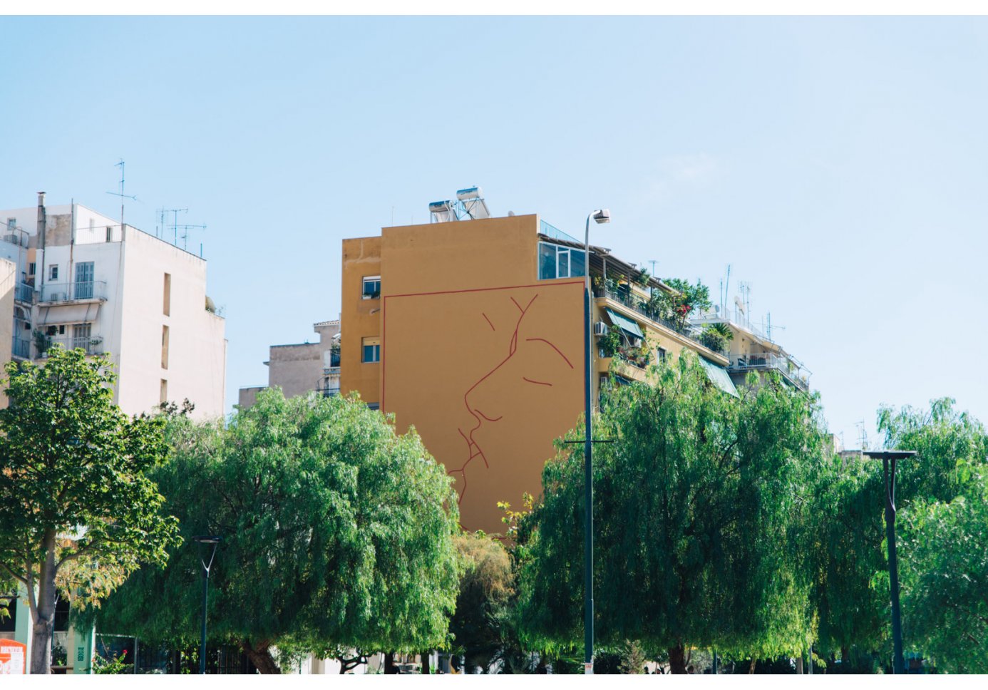 a mural on a building in a tree filled square depicting two people kissing