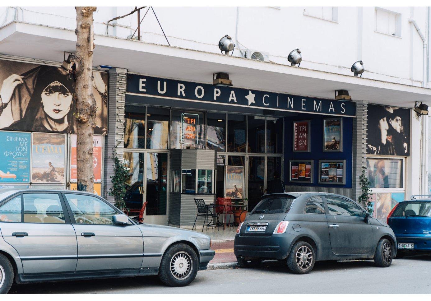 the entrance of a cinema, cars parked outside.