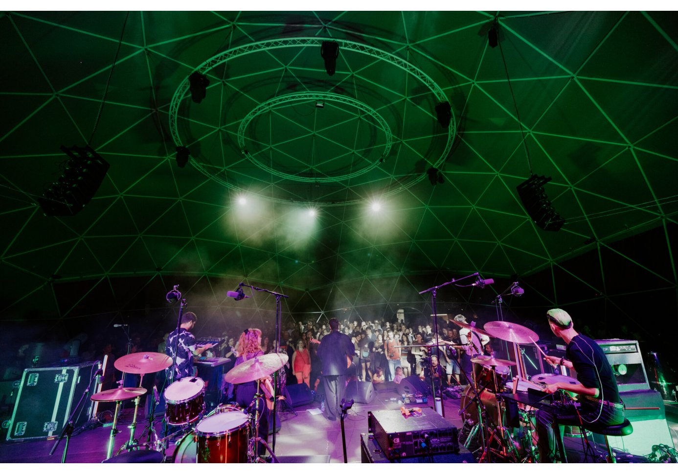 a band performing on stage under a dome-like structure, green and purple lighting