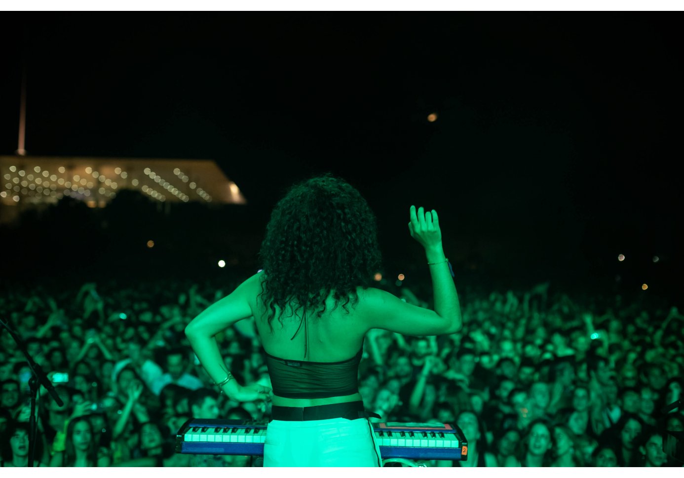 a woman playing the keys performing in front of a crowd, shot from behind