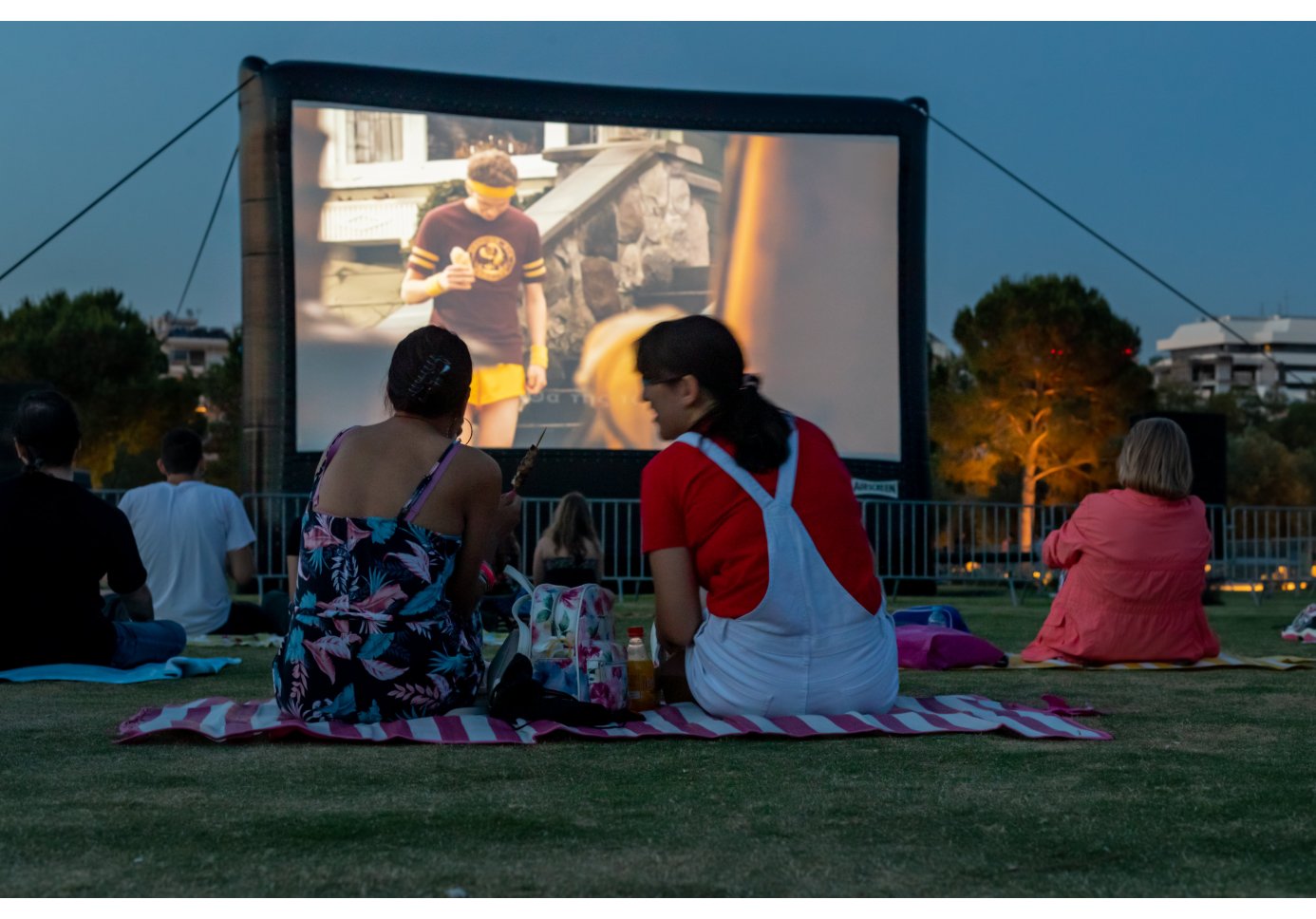 people sitting on the grass in a park, a film playing on a big screen