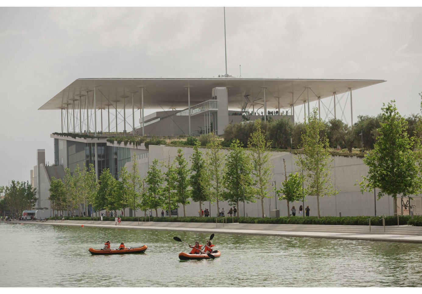 people kayaking in a man-made canal in front of a contemporary structure