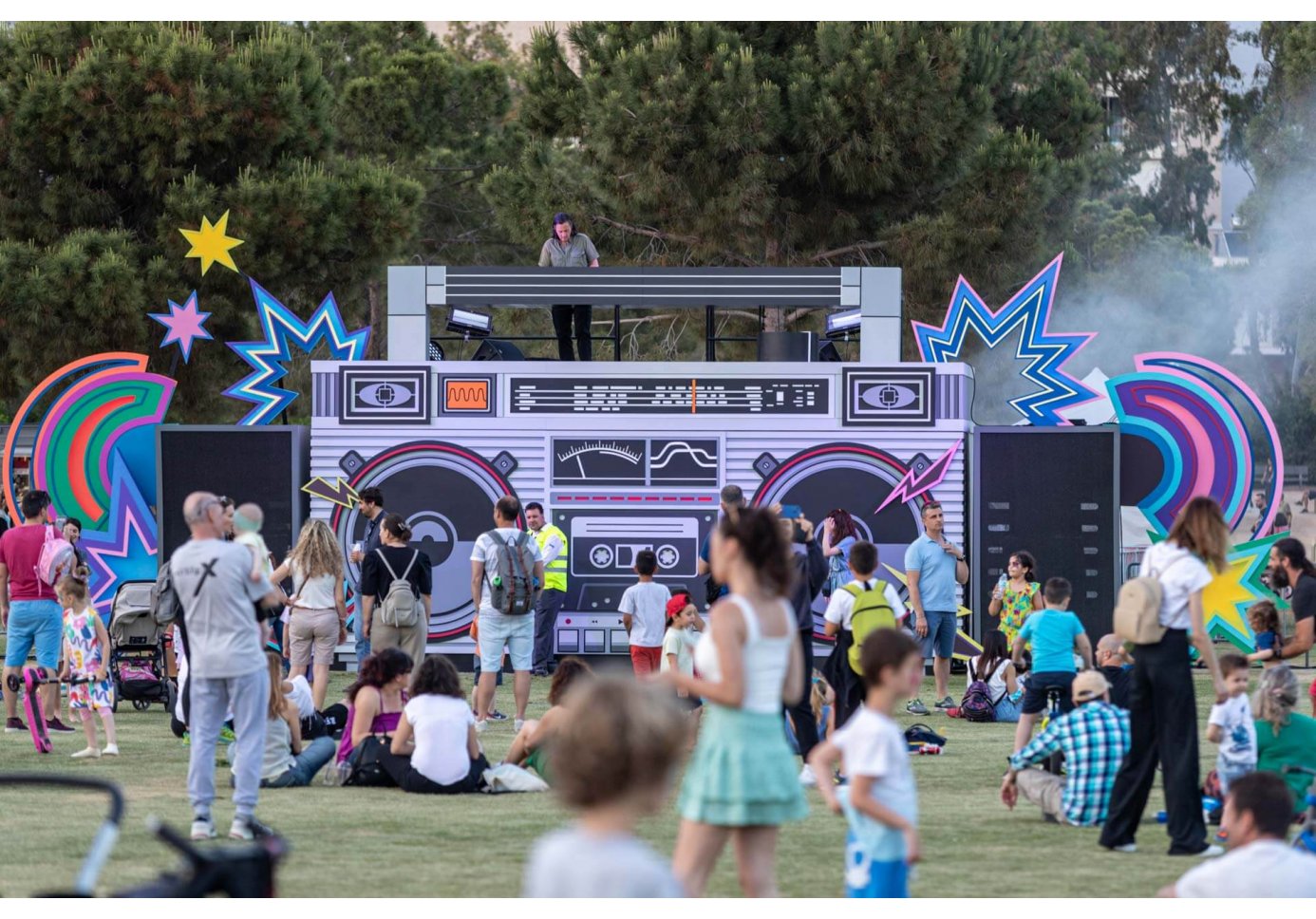 people gathered on a great lawn, a stage resembling a boom box where a dj plays music