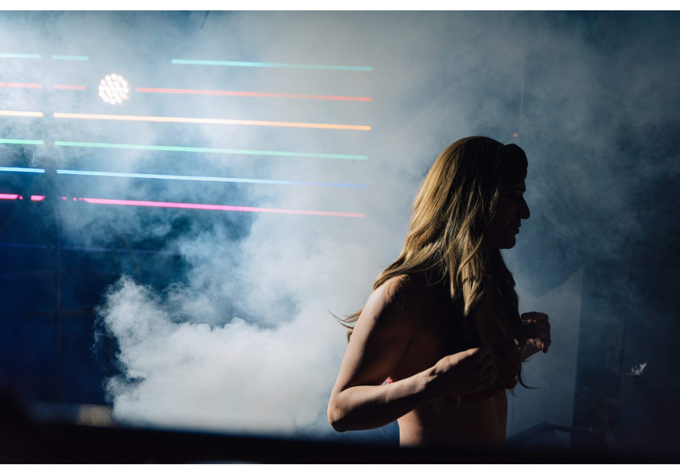 a drag performer on stage, rainbow lights behind them, smoke around them.