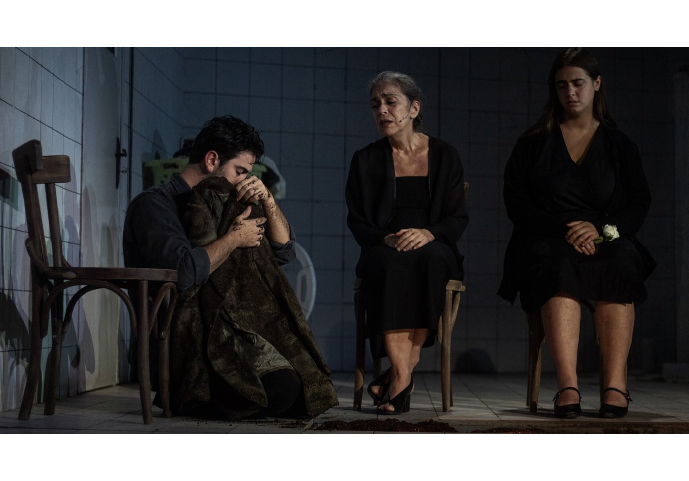 a man on the floor hugging a coat, two women sitting on chairs looking at him