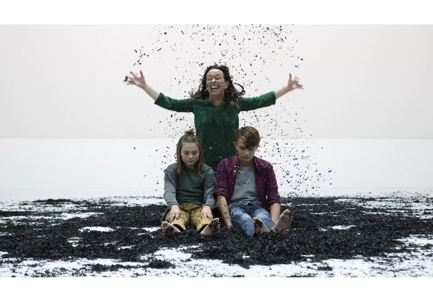 a woman throwing soil on two kids sitting in front of her