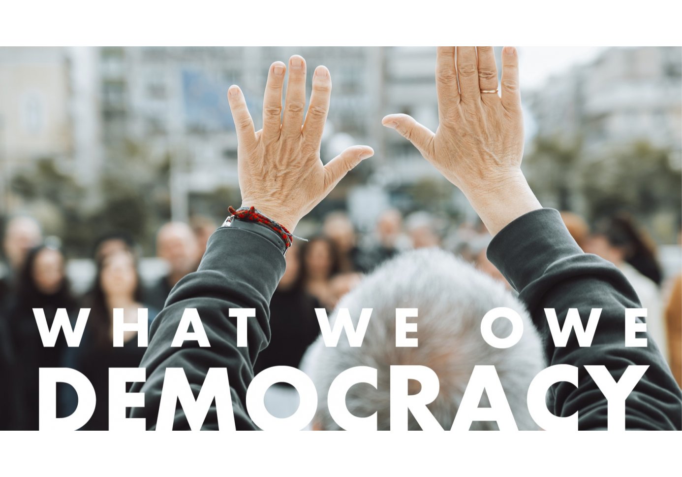 a man raising his hands in front of a crowd, lettering that reads "what we owe democracy"
