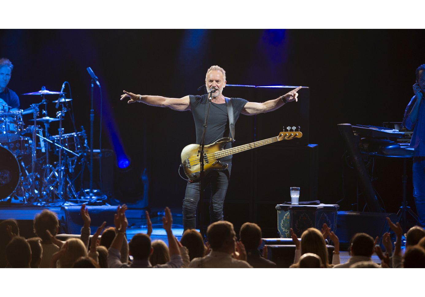 a man singing on stage with a guitar, crowd cheering