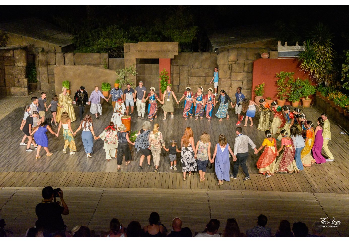 people in diverse dancing costumes dance in a circle