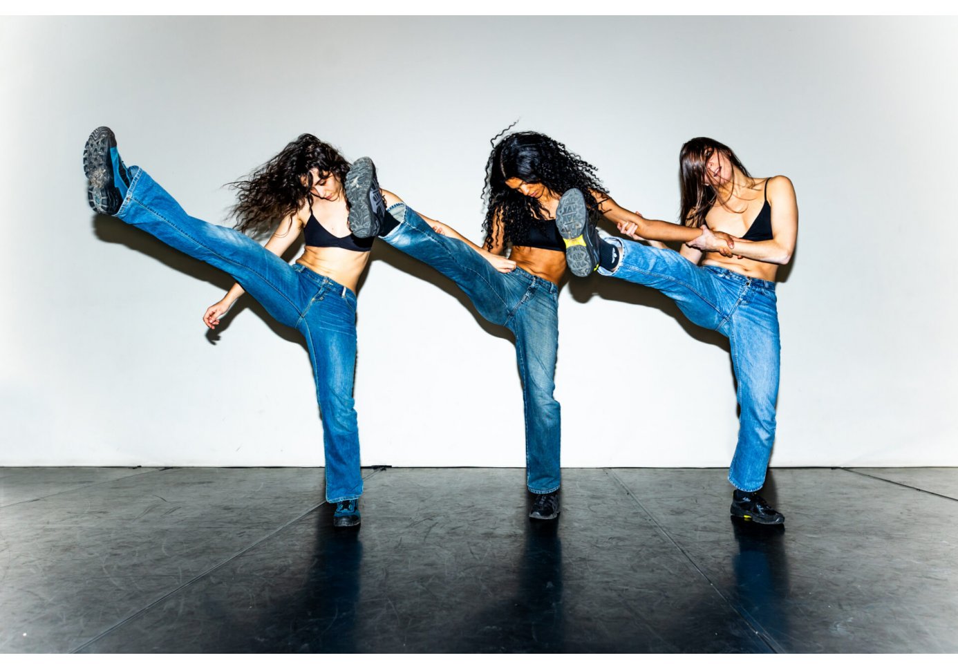three girls performing synchronized high kicks in a dance or performance setting.